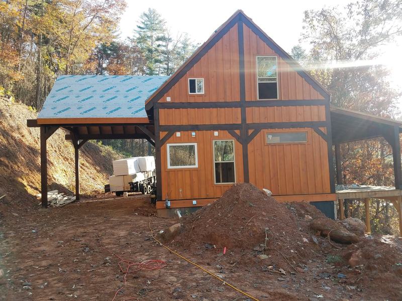 A stained board-and-batten house with dark timber trim and an attached carport. Opens larger.
